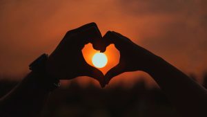 Hands forming a heart with a setting sun in middle