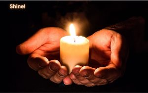 A person holding a glowing lantern in their hands, illuminating their face and the surrounding darkness