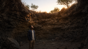 Young South African man looking towards the dawn from inside a dry, stone-lined pit.